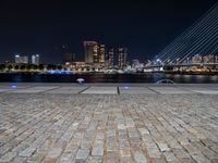 a city skyline and the night time view of a stone paved area in front of the water