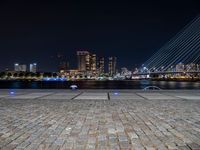 a city skyline and the night time view of a stone paved area in front of the water