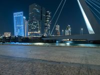 people are walking near a wide river next to some tall buildings at night time, as the city lights are on