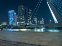 people are walking near a wide river next to some tall buildings at night time, as the city lights are on