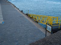 a large body of water with a yellow rail over it next to a brick walkway