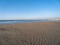 a large sandy beach next to the ocean on a clear day that shows some footprints in the sand