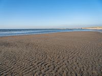 a large sandy beach next to the ocean on a clear day that shows some footprints in the sand