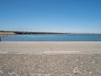 a paved parking lot next to the ocean and some buildings on a blue sky day