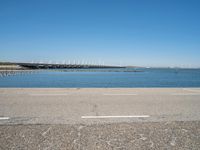 a paved parking lot next to the ocean and some buildings on a blue sky day