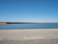 a paved parking lot next to the ocean and some buildings on a blue sky day