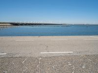 a paved parking lot next to the ocean and some buildings on a blue sky day