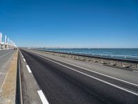 road beside the ocean with a beach in the distance and wind turbines in the background