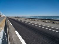 road beside the ocean with a beach in the distance and wind turbines in the background