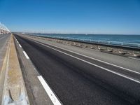 road beside the ocean with a beach in the distance and wind turbines in the background