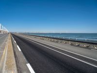 road beside the ocean with a beach in the distance and wind turbines in the background