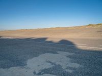 an empty road with a shadow cast on it with a car on the pavement next to it