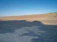 an empty road with a shadow cast on it with a car on the pavement next to it