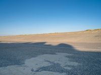 an empty road with a shadow cast on it with a car on the pavement next to it