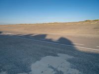 an empty road with a shadow cast on it with a car on the pavement next to it