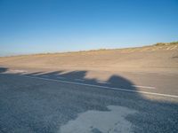 an empty road with a shadow cast on it with a car on the pavement next to it