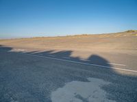 an empty road with a shadow cast on it with a car on the pavement next to it