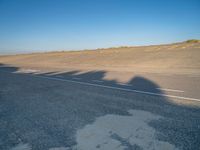 an empty road with a shadow cast on it with a car on the pavement next to it