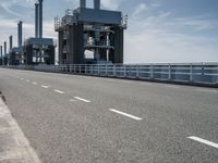 a man riding a bicycle on a road next to a sea view and industrial area