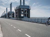 a man riding a bicycle on a road next to a sea view and industrial area