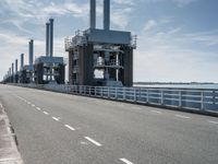 a man riding a bicycle on a road next to a sea view and industrial area