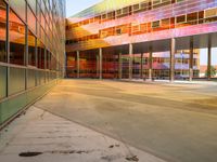 a bright yellow orange and red building is reflected in the windows of its nearby glassy building