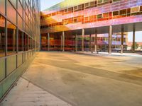 a bright yellow orange and red building is reflected in the windows of its nearby glassy building