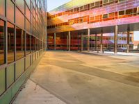 a bright yellow orange and red building is reflected in the windows of its nearby glassy building