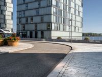 an empty road with two office buildings on the left and two plants on the right side