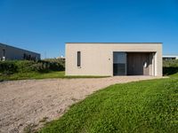 an empty concrete structure sitting in grass and gravel next to a beach house on the sand