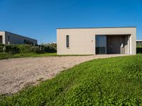 an empty concrete structure sitting in grass and gravel next to a beach house on the sand