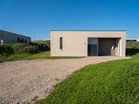 an empty concrete structure sitting in grass and gravel next to a beach house on the sand