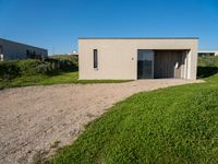 an empty concrete structure sitting in grass and gravel next to a beach house on the sand