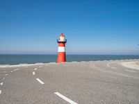 a red and white lighthouse is on the side of the road by the water, overlooking a calm beach