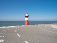 a red and white lighthouse is on the side of the road by the water, overlooking a calm beach