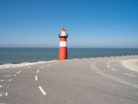 a red and white lighthouse is on the side of the road by the water, overlooking a calm beach