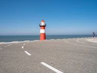 a red and white lighthouse is on the side of the road by the water, overlooking a calm beach