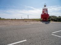 a red and white lighthouse on the side of the road with grass in front of it