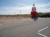 a red and white lighthouse on the side of the road with grass in front of it