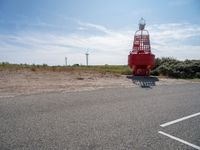 a red and white lighthouse on the side of the road with grass in front of it