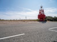 a red and white lighthouse on the side of the road with grass in front of it