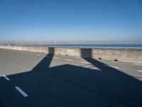 a bridge over the ocean with construction equipment in the background and two people walking on it