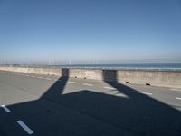 a bridge over the ocean with construction equipment in the background and two people walking on it