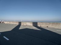 a bridge over the ocean with construction equipment in the background and two people walking on it