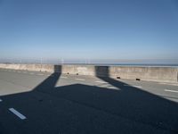 a bridge over the ocean with construction equipment in the background and two people walking on it