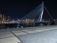 the city skyline behind the bridge is lit up at night, while people walking along the sidewalk look on