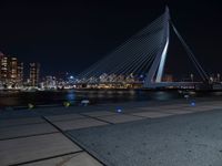 the city skyline behind the bridge is lit up at night, while people walking along the sidewalk look on