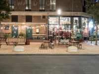 a building with a bunch of tables and benches near by it at night outside eating at the sidewalk