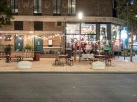 a building with a bunch of tables and benches near by it at night outside eating at the sidewalk