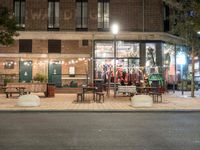 a building with a bunch of tables and benches near by it at night outside eating at the sidewalk